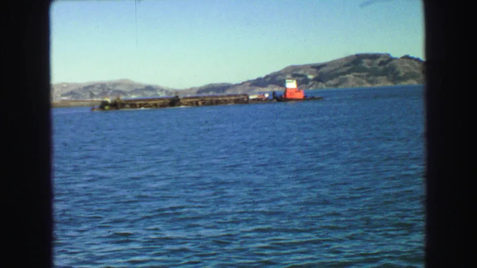 Vancouver-area ferry view from 1968 showing open blue water, distant hills and a red-and-white vessel or structure along the shore.