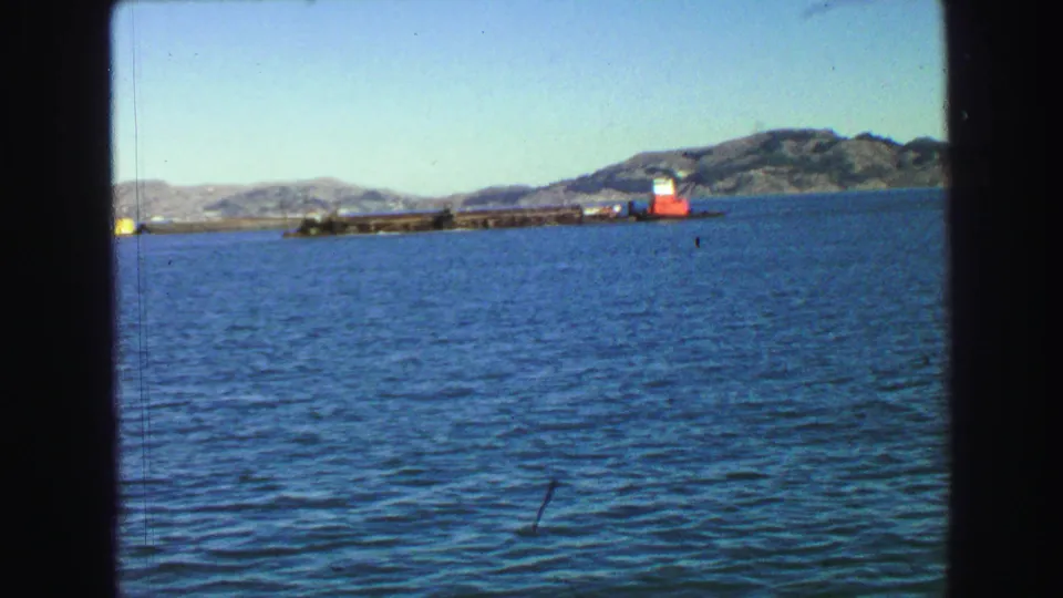 1968 Vancouver-area 8mm frame showing blue water, distant hills, and a long harbor structure with a red-and-white marker.