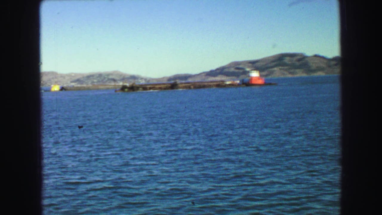 Distant waterway with a low pier, red-and-white marker, hills, and open sky.