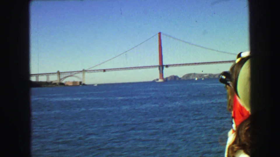 Golden Gate Bridge viewed from a boat across blue water, with a passenger partly entering the right edge of the 1968 8mm frame.
