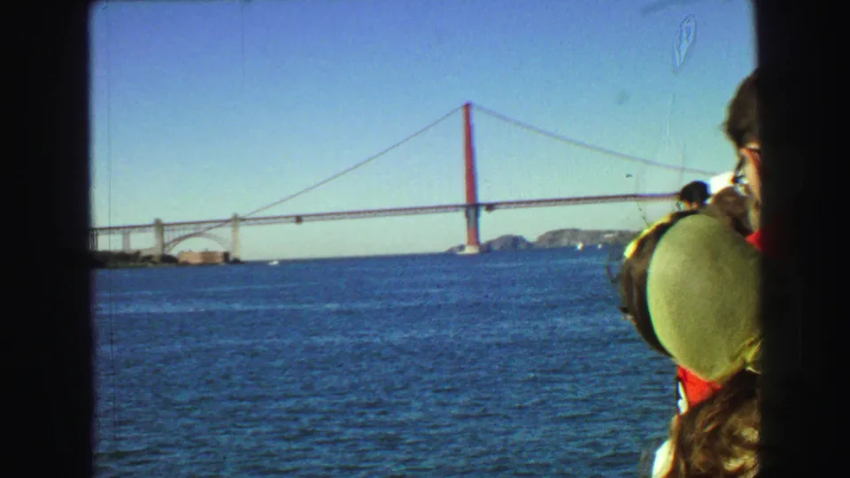 1968 8mm boat view of the Golden Gate Bridge, with several passengers in the foreground looking across the water.