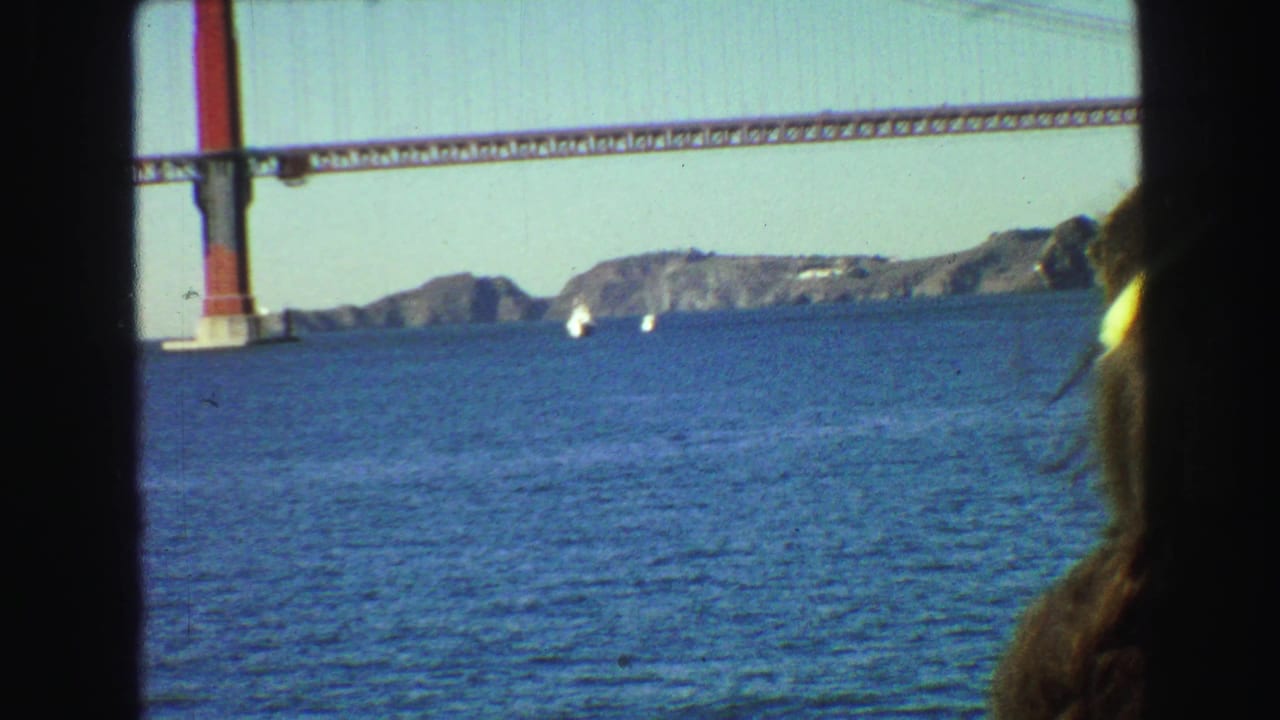 A red suspension bridge crosses blue water with rocky shoreline beyond.