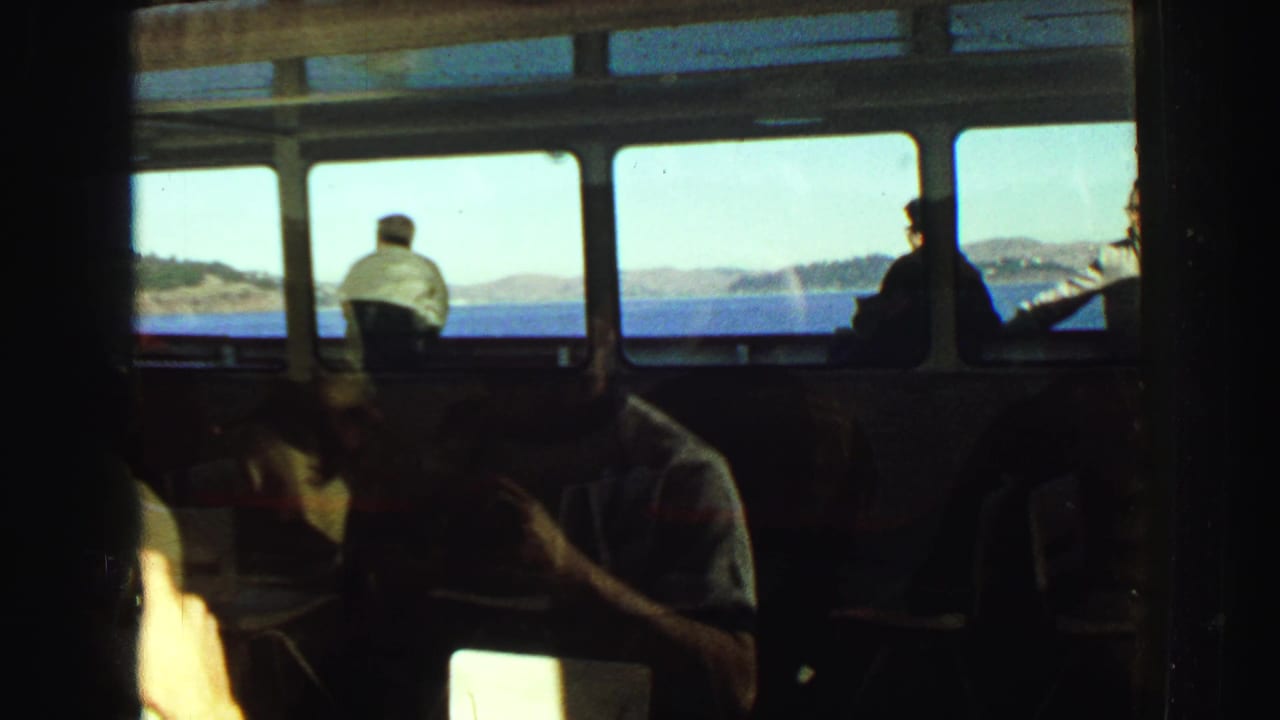 Dark boat interior with passengers in shadow and bright sea and coastline visible through the windows.