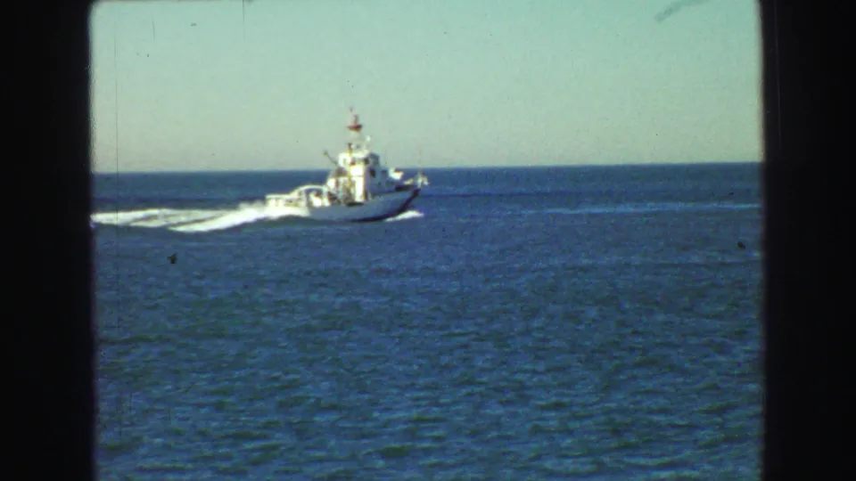 A white motorboat crosses blue coastal water in 1968 Vancouver-area home-movie footage, leaving a bright wake with horizon and sky behind it.