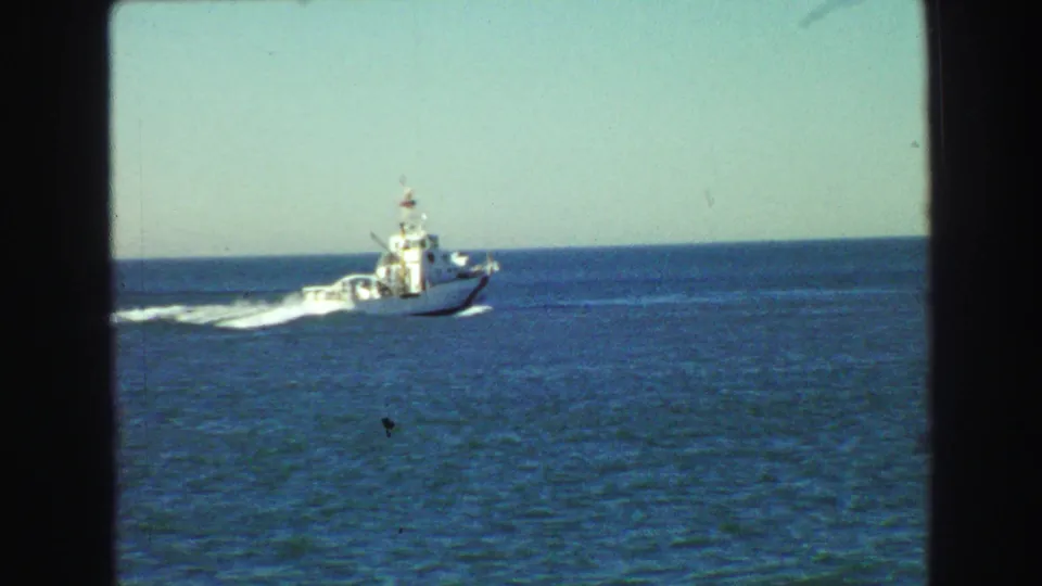 The passing white motorboat continues across the blue water, framed by a simple horizon and pale sky in the 1968 Vancouver-area 8mm footage.