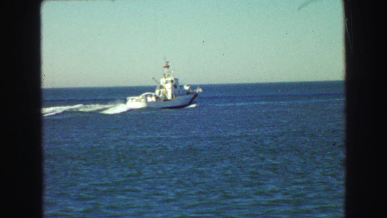 White boat farther across blue water with wake trailing behind.