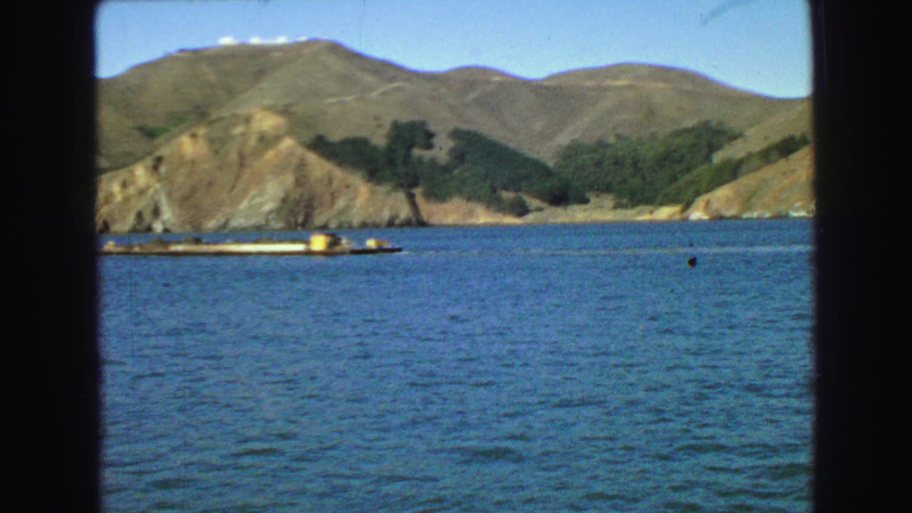 Mountainous coastline across blue water seen through dark boat-window framing.