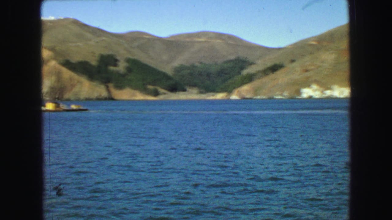 Blue water and hilly shoreline with dark vertical boat framing in the foreground.
