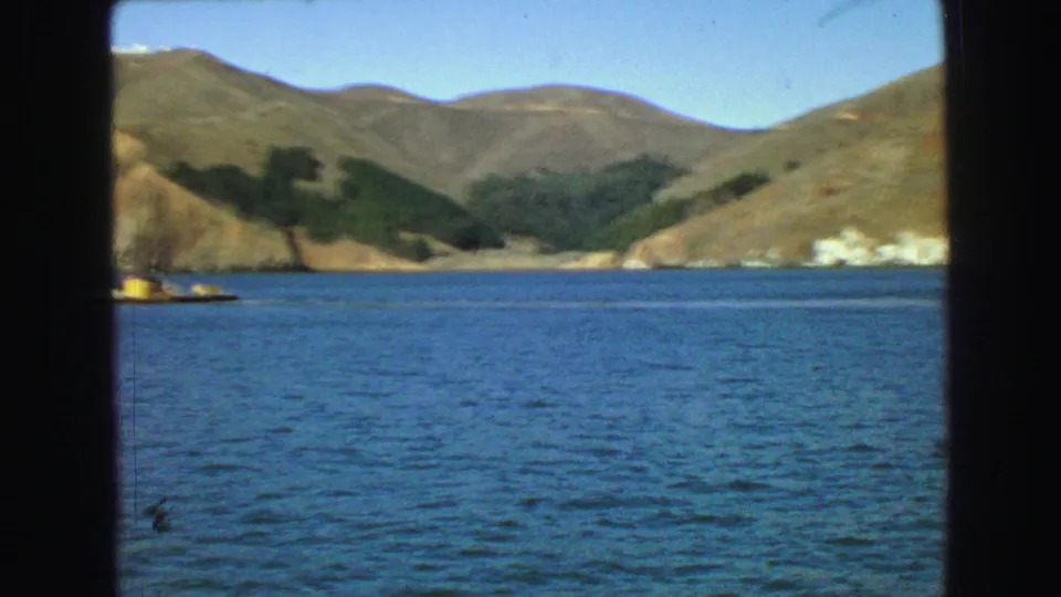 Coastal hills and blue water near Vancouver in 1968, viewed from a boat with dark vertical framing at the sides.