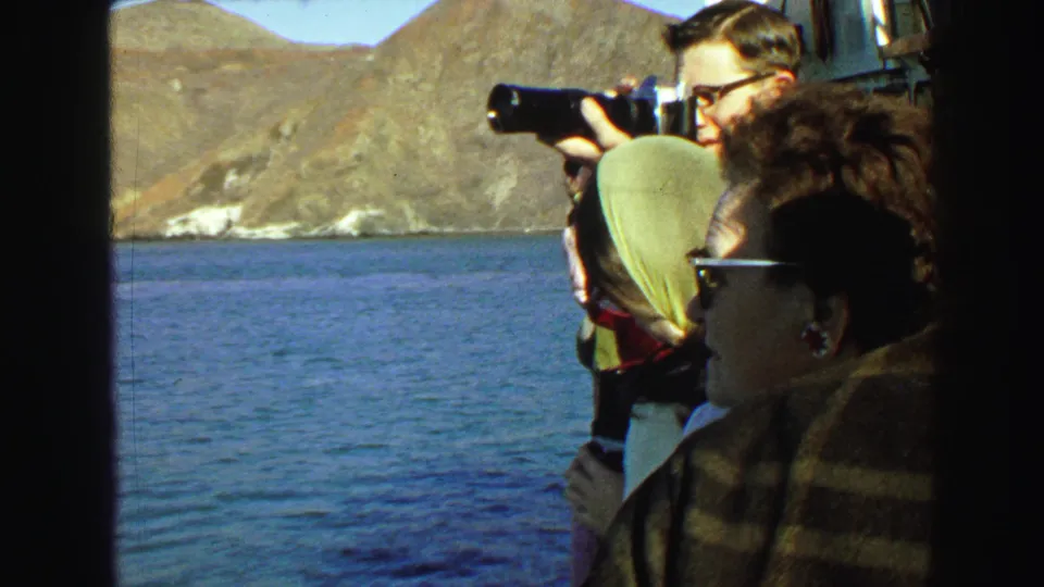 Tourists aboard a boat near Vancouver in 1968 look toward the water and hills as a man with glasses photographs the view.