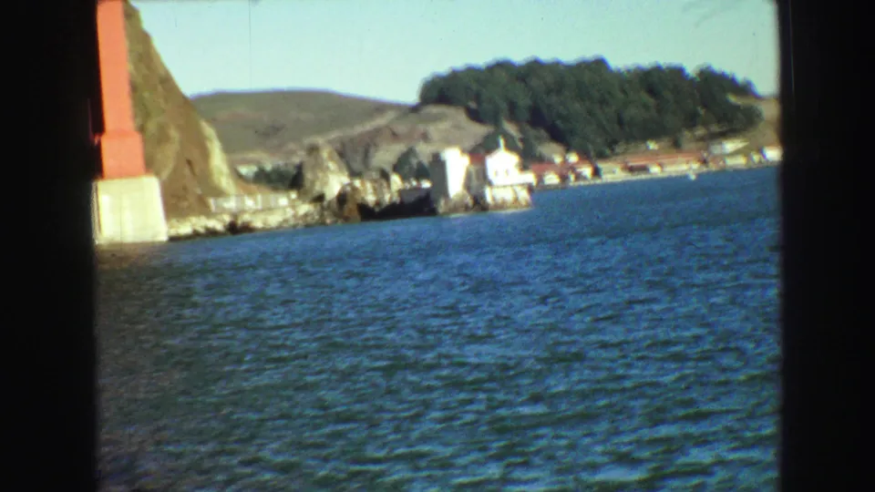 Final frame looking across San Francisco Bay toward shoreline buildings and trees, with a red bridge support partly visible at left.