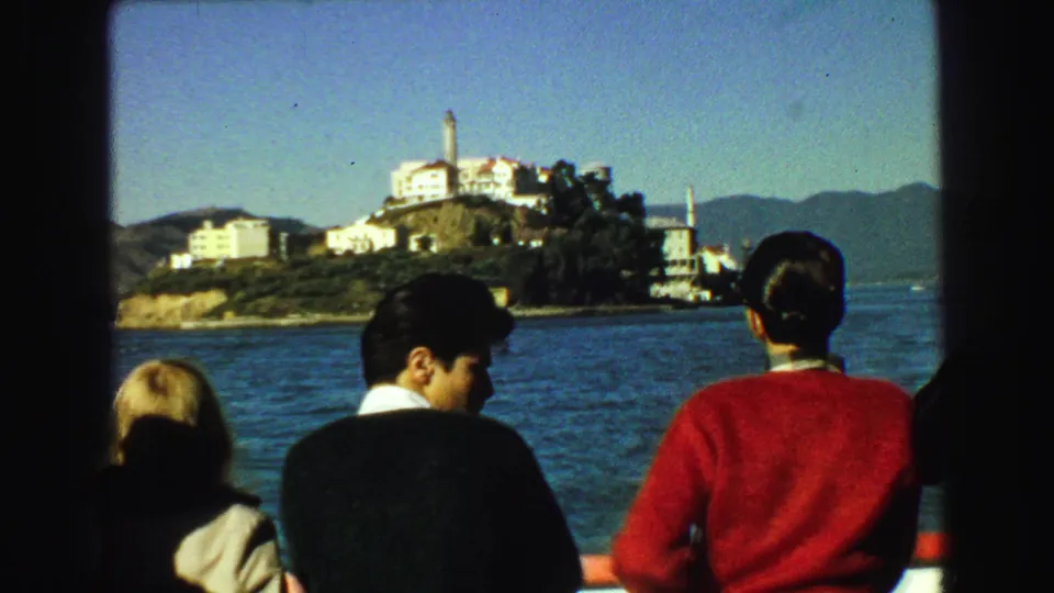 1968 8mm frame of Alcatraz Island across San Francisco Bay, viewed from a boat with passengers in the foreground.