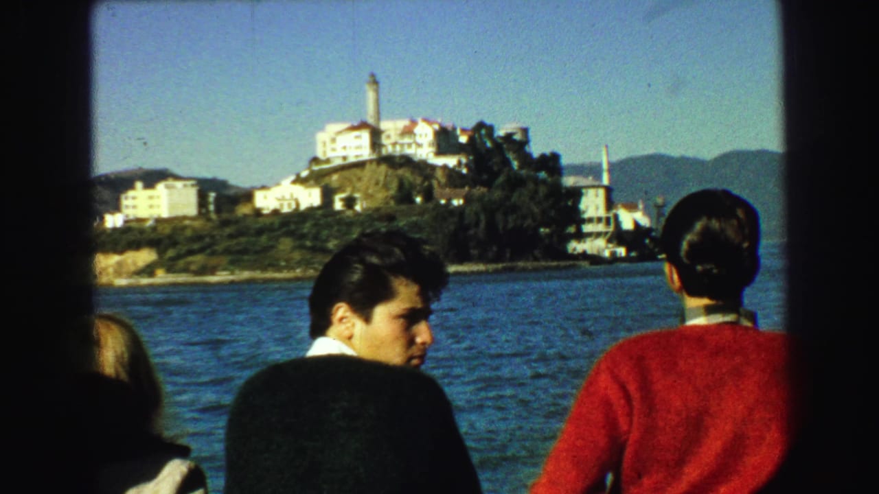 Tourists on a boat look toward Alcatraz Island across blue water.