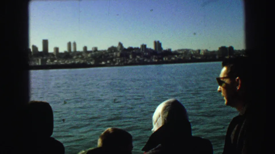 1968 8mm frame of tourists on a boat with San Francisco's skyline and waterfront visible across the water.