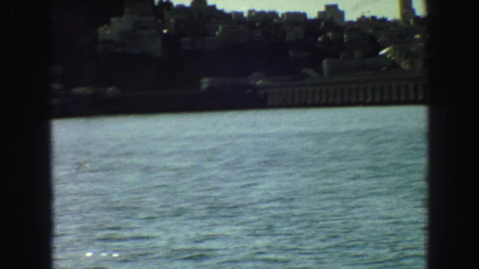 Distant Vancouver shoreline and hillside buildings viewed across rippling water, partly obscured by dark window-like edges.