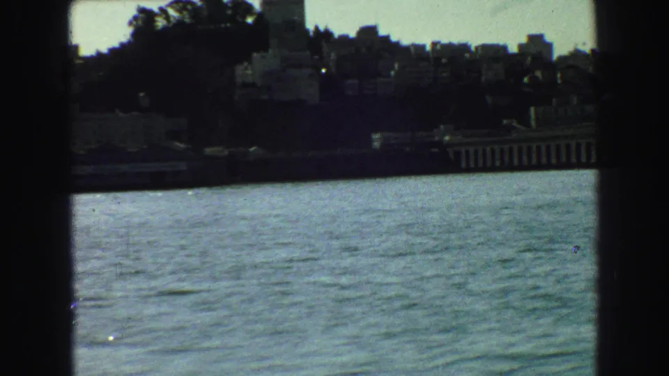 1968 Vancouver skyline segment with hillside buildings and waterfront architecture seen across blue-green water through dark framing.