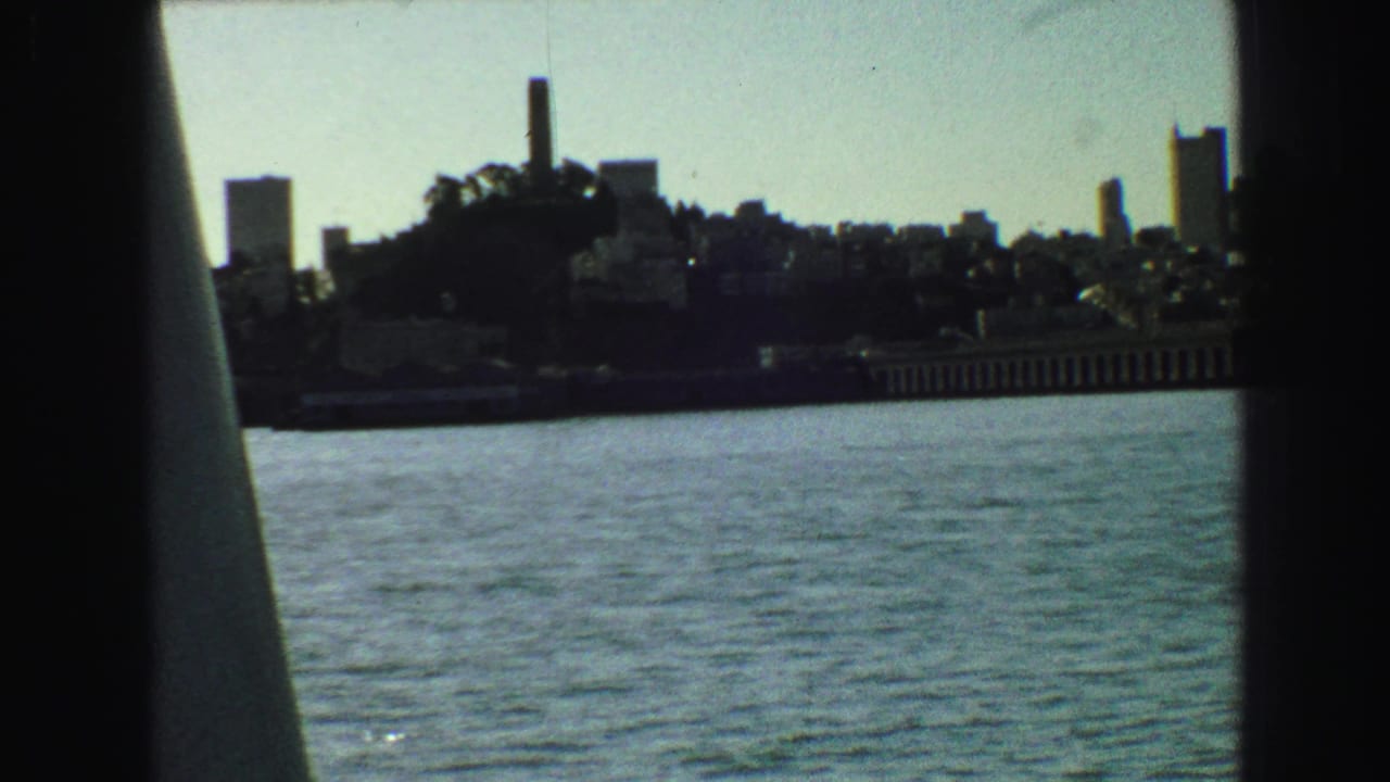 Distant waterfront skyline seen across water through dark boat framing.