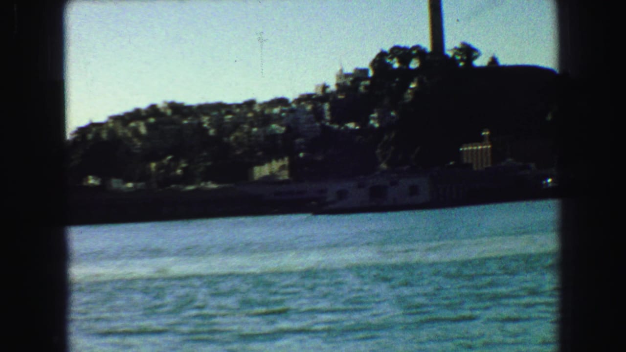 Waterfront seen through a dark boat window with hillside trees and low shoreline buildings.