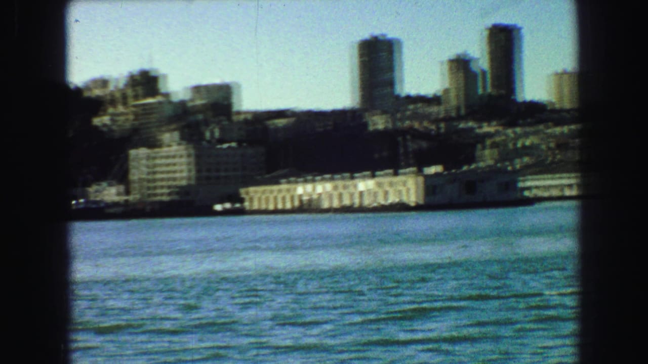 Distant city skyline across blue water, framed by dark vertical edges.