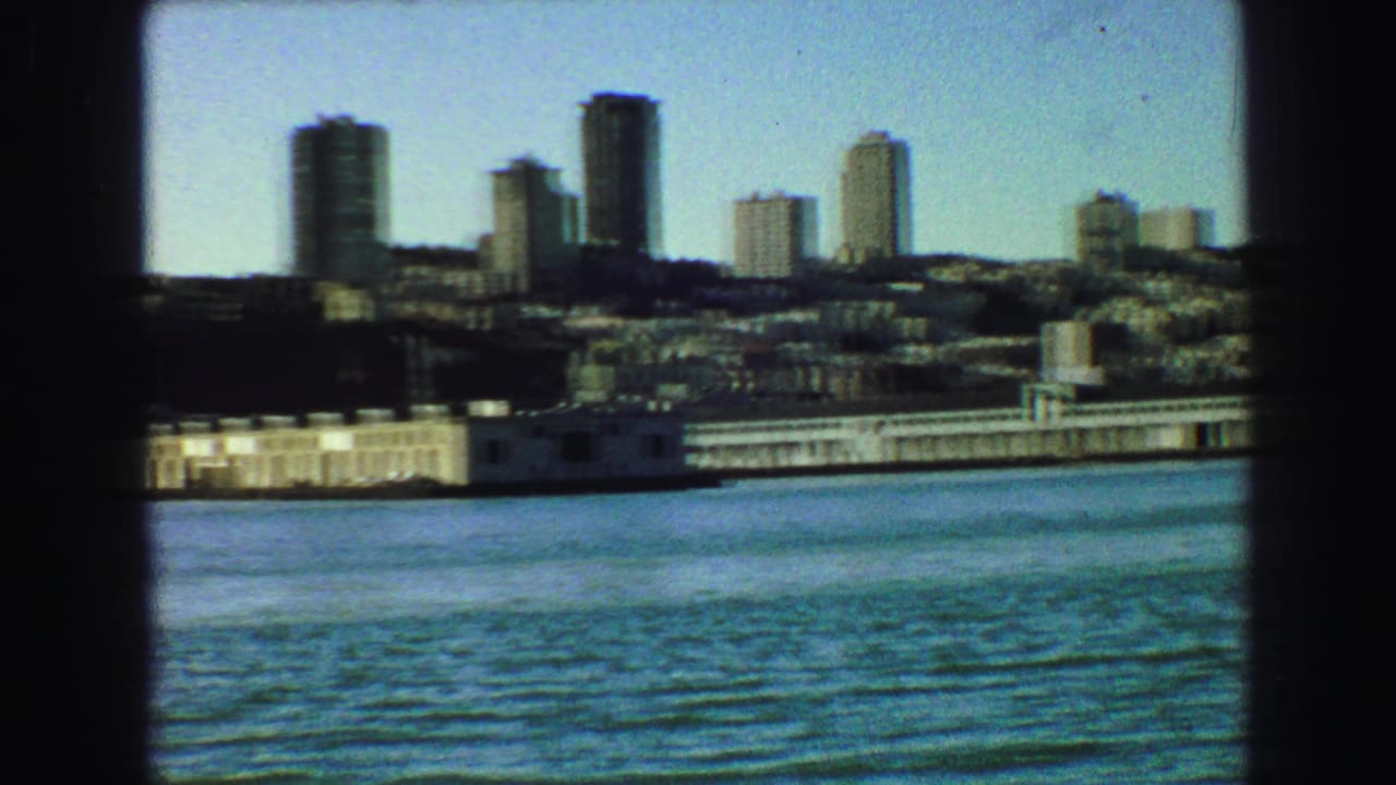 Urban waterfront skyline across rippled water with dark frame edges.