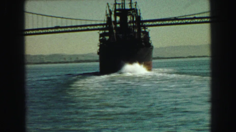 1968 Vancouver 8mm frame showing the stern of a large ferry beneath a suspension bridge, with wake, distant land, and window framing.
