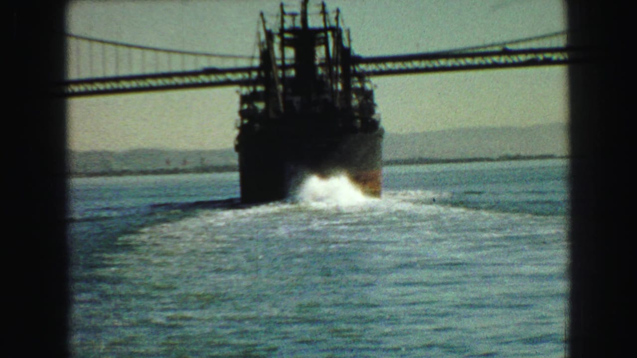 Large cargo ship passing beneath a suspension bridge over open water.
