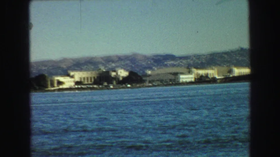 1968 Vancouver waterfront view from the water, with low buildings along the shore and hills in the background.