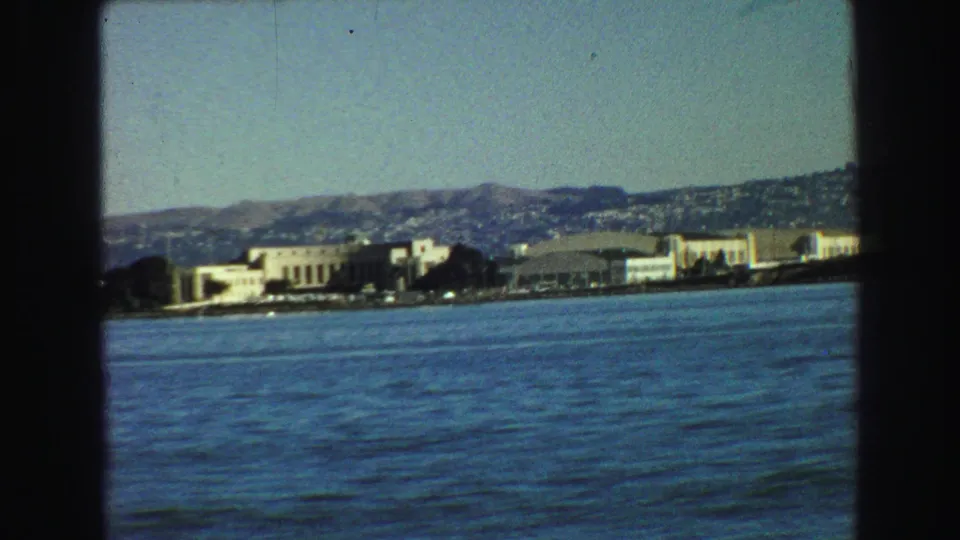 Vancouver-area 1968 home-movie view of a distant shoreline, low waterfront buildings, hills, and rippled bay water.