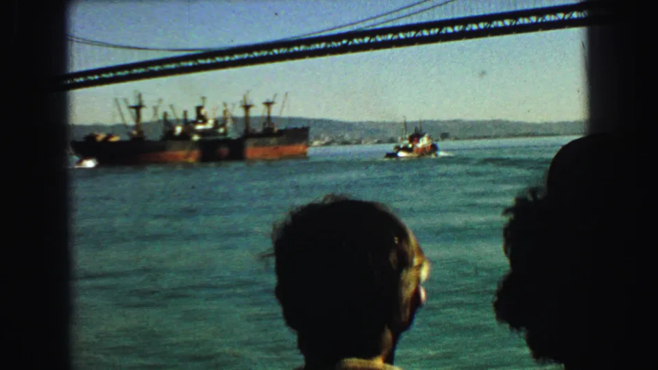Passenger silhouettes watch a tugboat and cargo ship in Vancouver harbor, with a bridge line crossing the upper frame.
