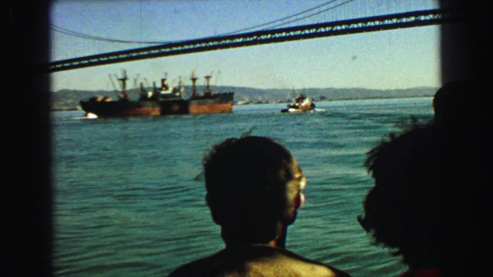 Vancouver harbor scene from 1968 with bridge cables above, a cargo ship and tugboat beyond, and passengers watching in silhouette.