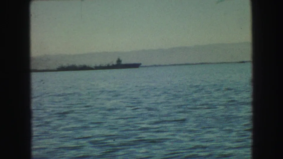 A distant military-style vessel appears on Vancouver harbor water in this 1968 8mm home-movie frame, with hills and haze in the background.
