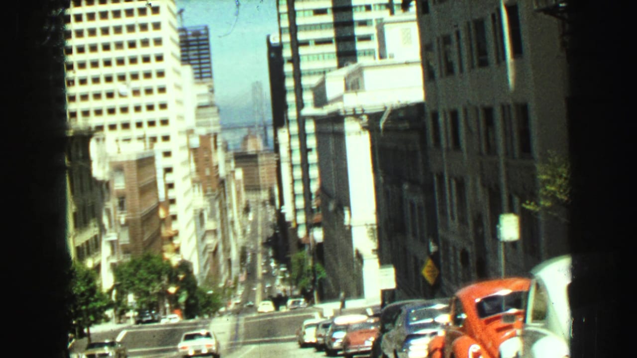 1968 Vancouver street view looking downhill between tall buildings, with cars and a distant bridge visible.