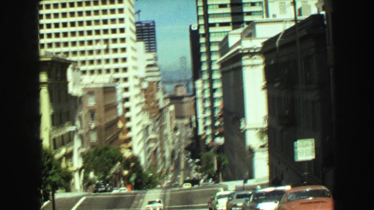 1968 Vancouver downtown view with tall buildings, parked cars, street signs, and a distant bridge near the waterfront.