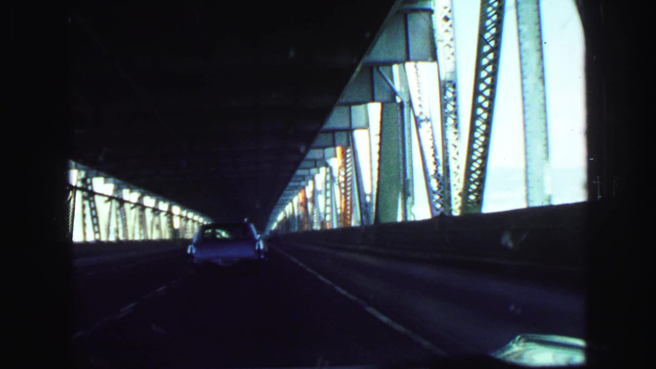 Car continues through a dark steel bridge with bright truss panels at the side.