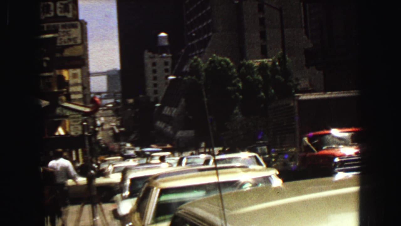 1968 Vancouver street view from a moving car, with mid-century traffic, tall buildings, signage, and distant pedestrians visible.