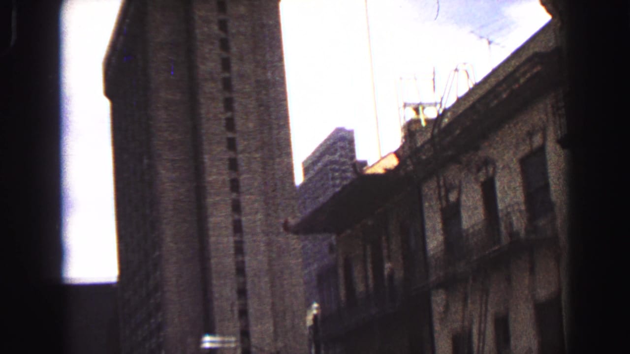 Handheld 1968 Vancouver upward pan showing a tall tower, older low-rise facade, rooftop antennas, and pale sky.