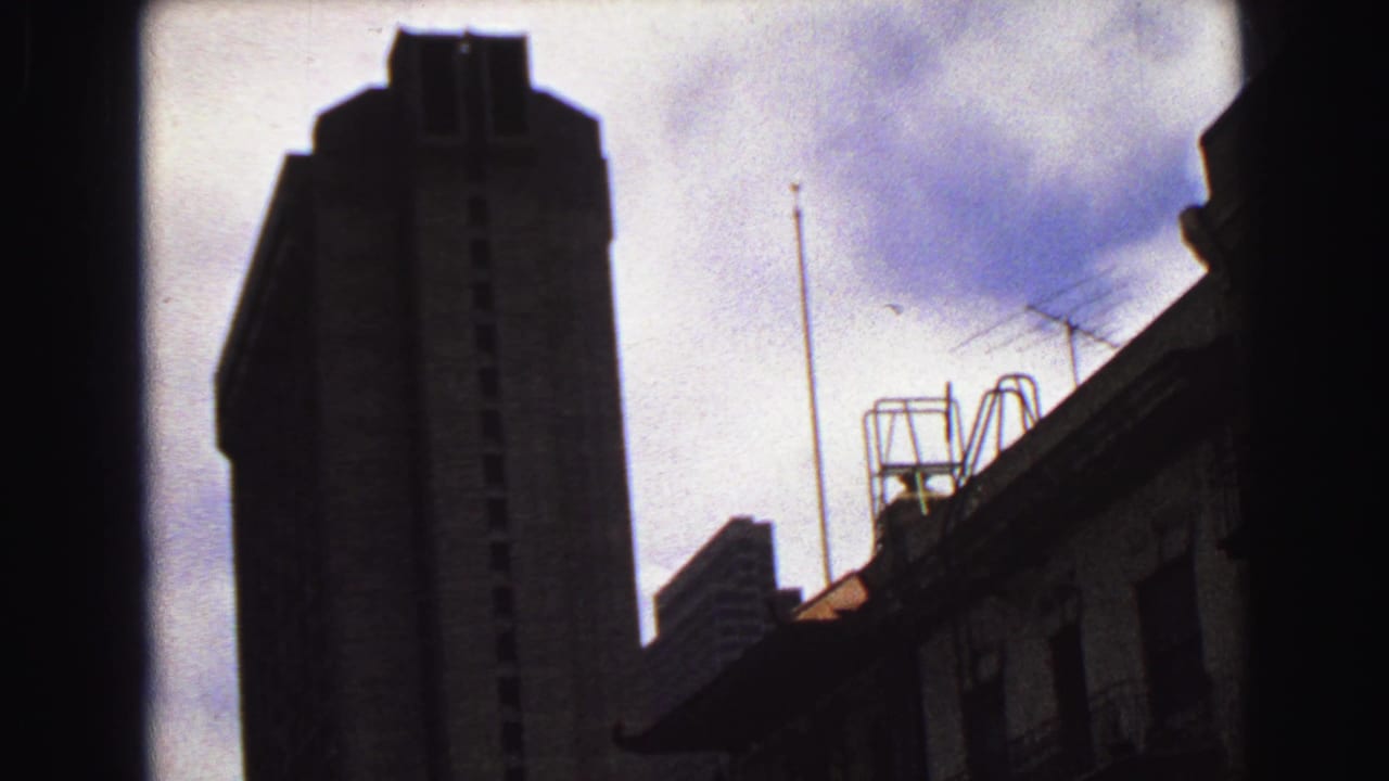 1968 Vancouver upward view with a dark tower silhouette, rooftop antennas, a smaller roofline, and cloudy sky.