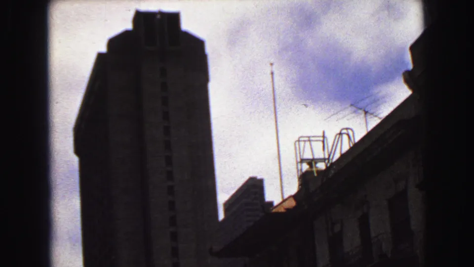 1968 Vancouver upward view with a dark tower silhouette, rooftop antennas, a smaller roofline, and cloudy sky.