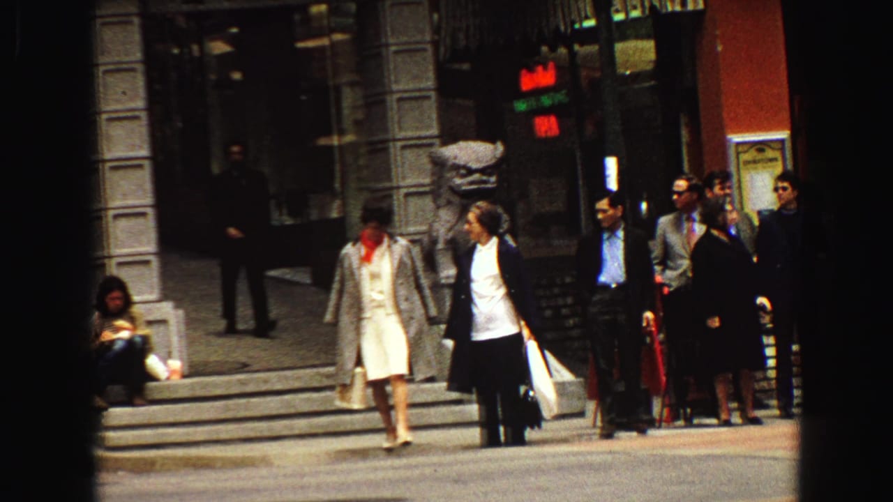 Pedestrians wait near storefront steps on a city street.
