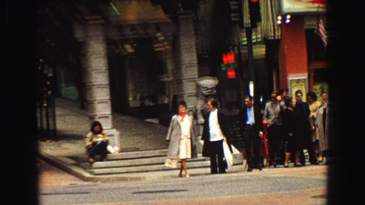1968 Vancouver street corner with pedestrians waiting beside storefronts and a vertical dark film edge crossing the frame.