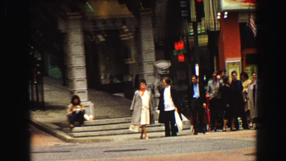 1968 Vancouver street corner with pedestrians waiting beside storefronts and a vertical dark film edge crossing the frame.