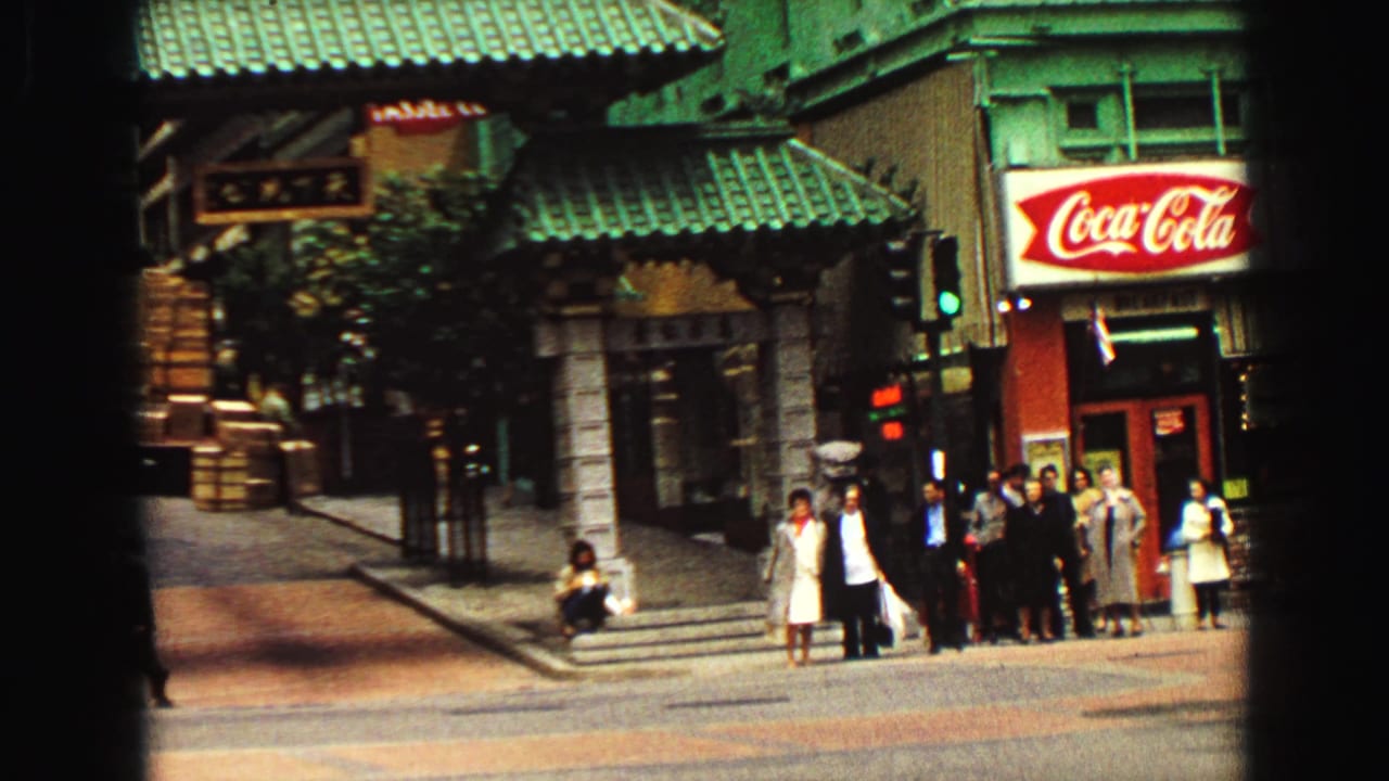 1968 Vancouver street scene showing pedestrians below green tiled roofing, storefronts, a traffic light, and a Coca-Cola sign.