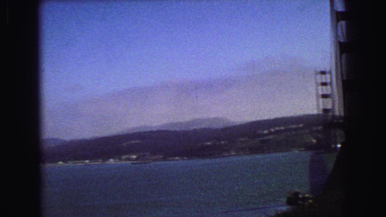 Partial suspension bridge tower over blue water with distant hills and shoreline.