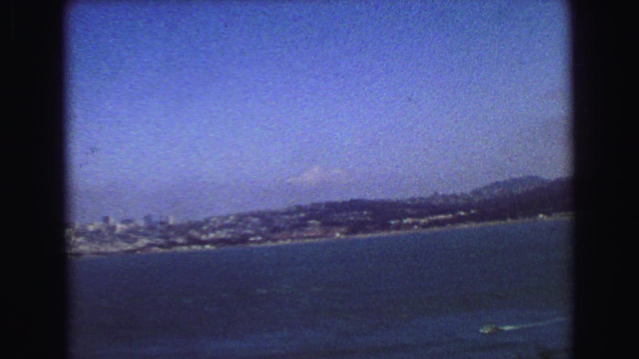 1968 8mm travel frame showing a distant urban waterfront skyline across the bay, backed by low hills.