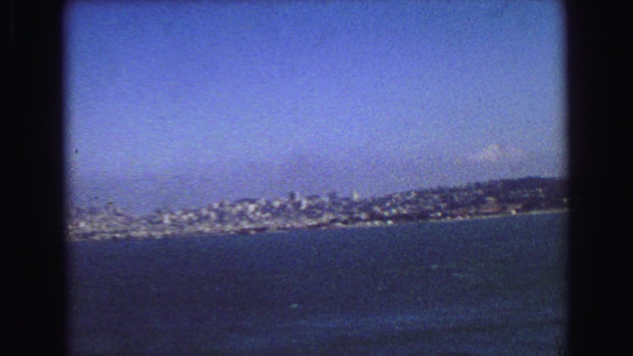 1968 8mm frame with a broad bay view toward dense shoreline buildings and low hills in the distance.