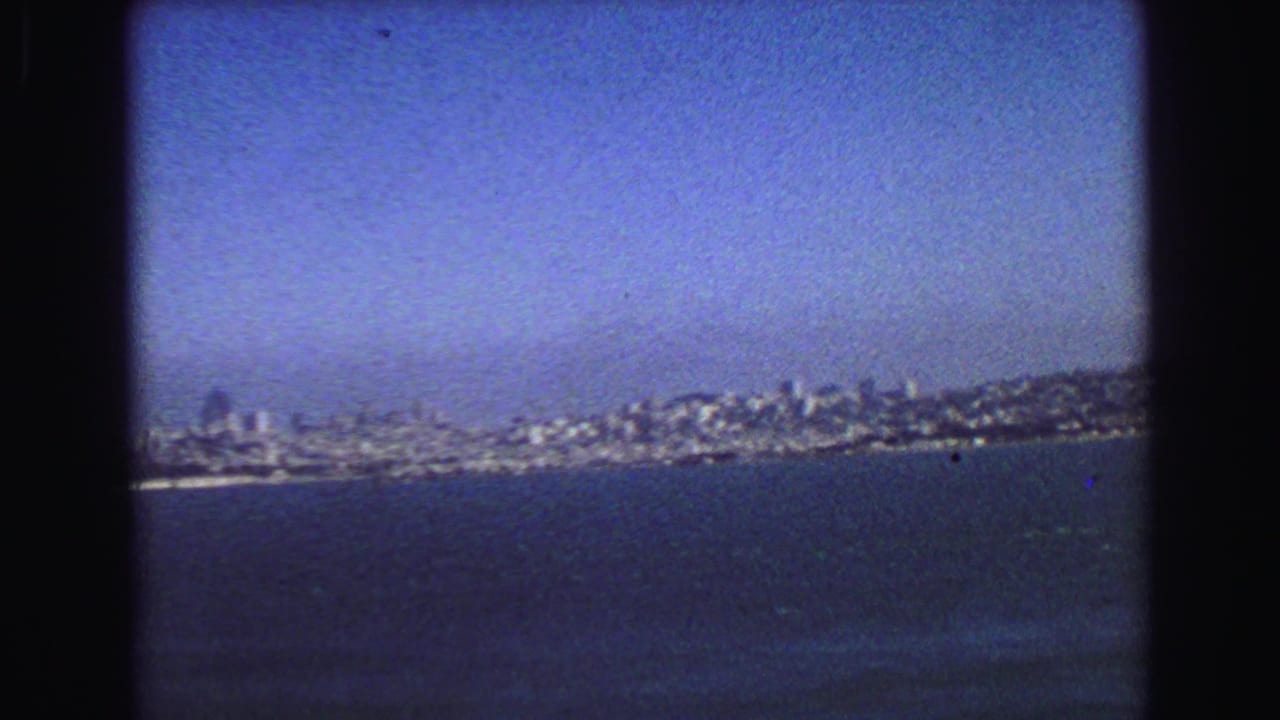 Distant city skyline across dark blue water under a clear sky.