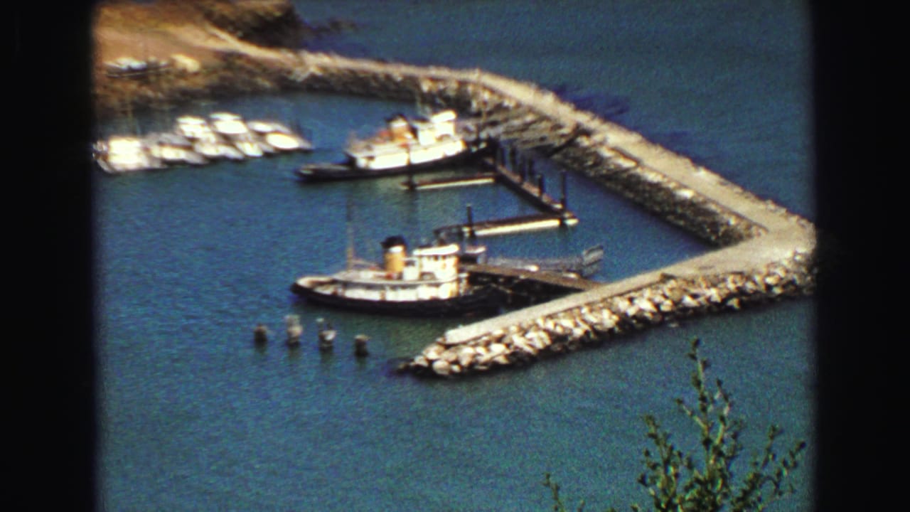Closer 1968 Vancouver harbor view with docked boats, piers, and a larger tug-like vessel near a rock breakwater.