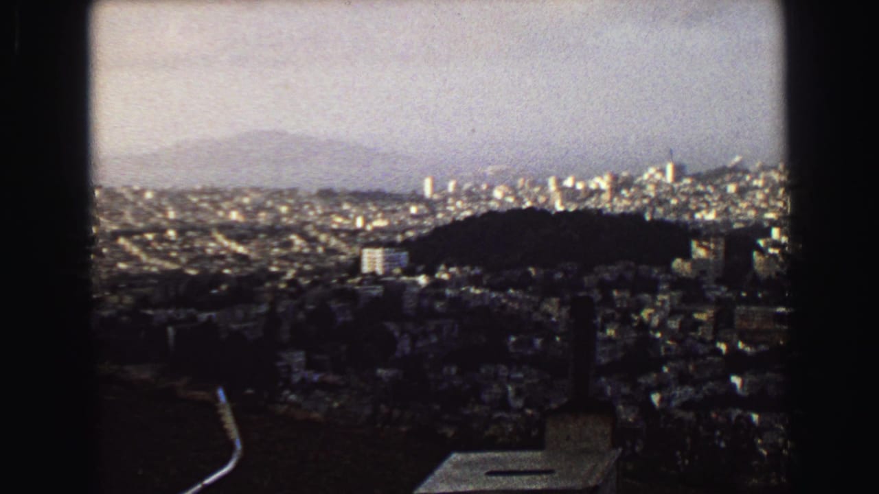 Elevated city view with hills, dense buildings, and a hazy skyline.