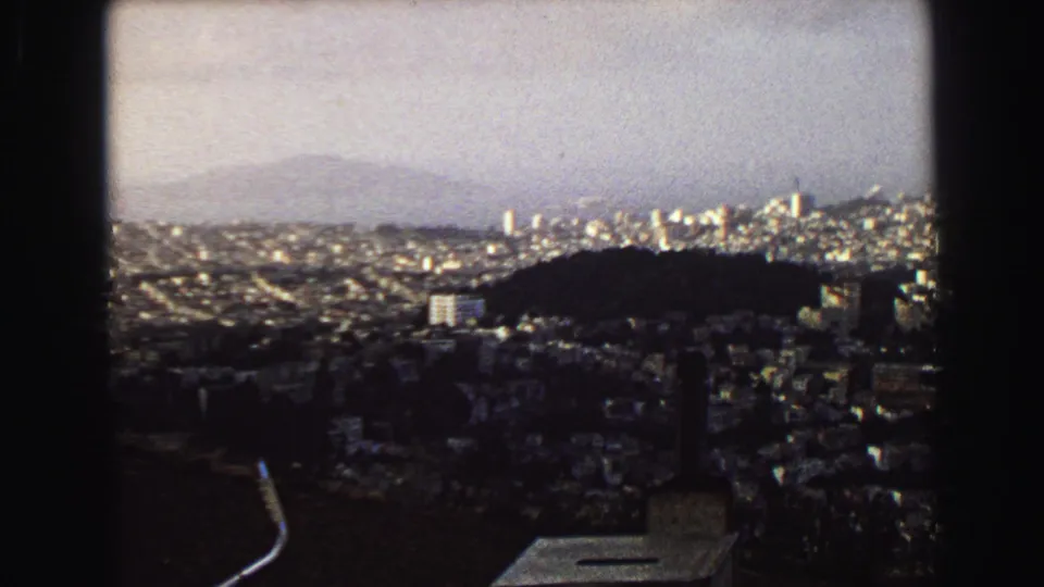Elevated 1968 view over Vancouver with hillside foreground, dense city blocks, distant high-rises, and a hazy sky.