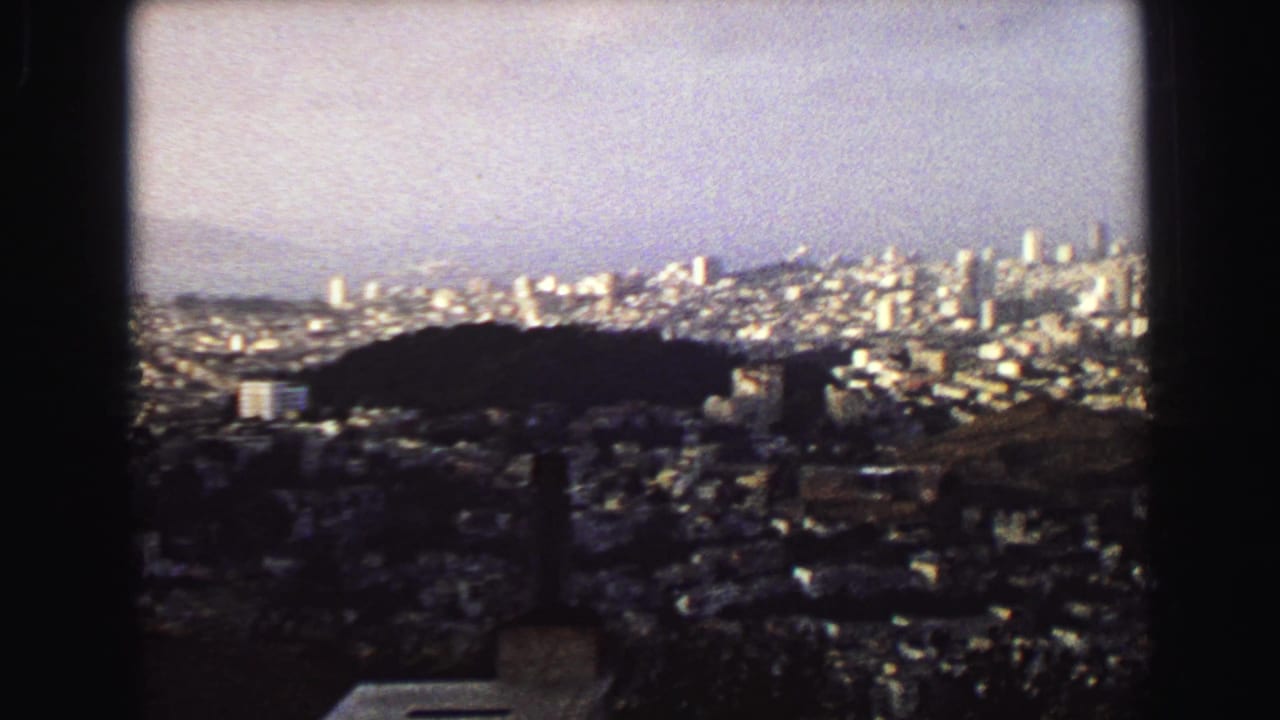 1968 Vancouver panorama from above, showing a dark wooded hill, dense neighborhoods, and distant bright city towers.